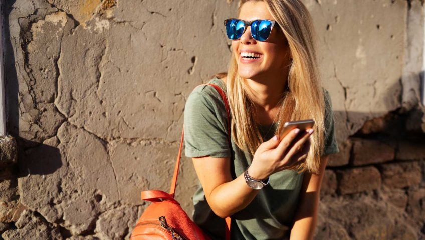 A woman in sunglasses is holding a cell phone.