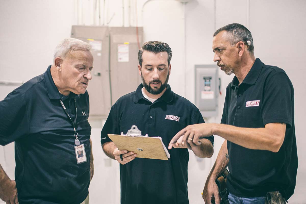 Three men looking at a clipboard in a warehouse.