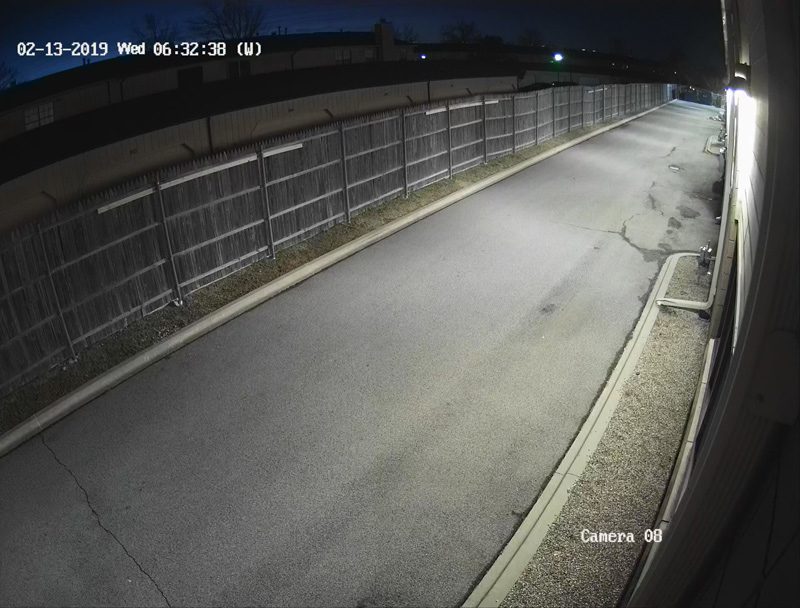 A security camera captures an empty road at night.