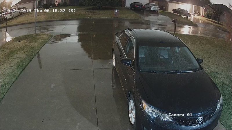 A black car is parked in a wet driveway.