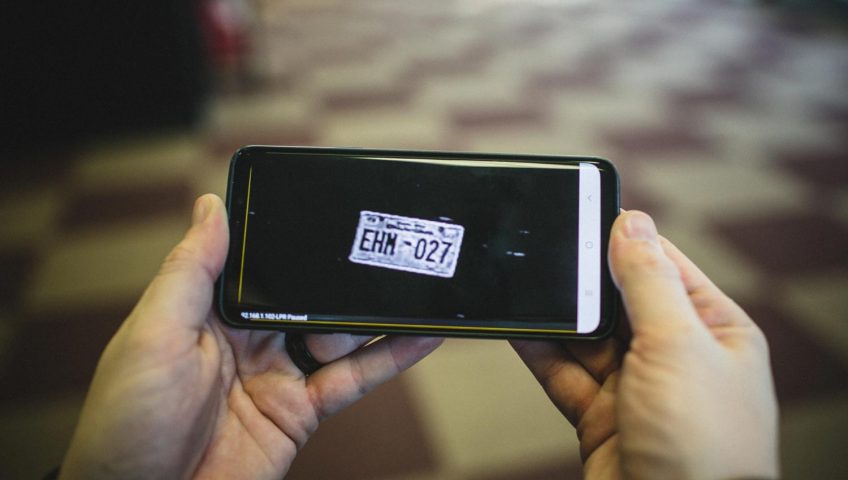 A person holding a phone with a plate number on screen